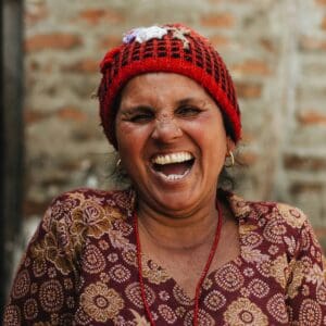 A woman with a red hat and necklace laughing.